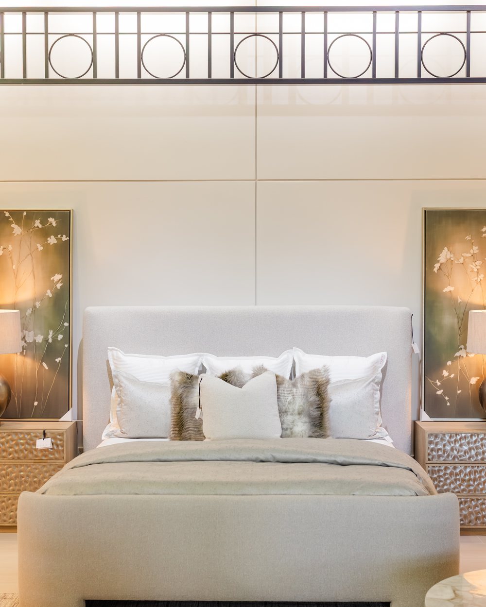 An upholstered Bernhardt bed layered in ivory beneath the Interiors gallery sign