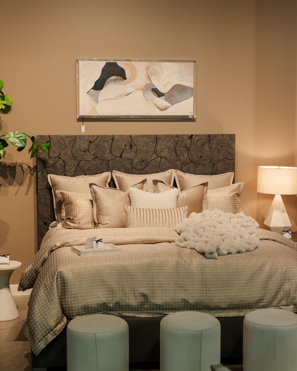 A layered upholstered bed with a woven headboard and mint velvet poufs
