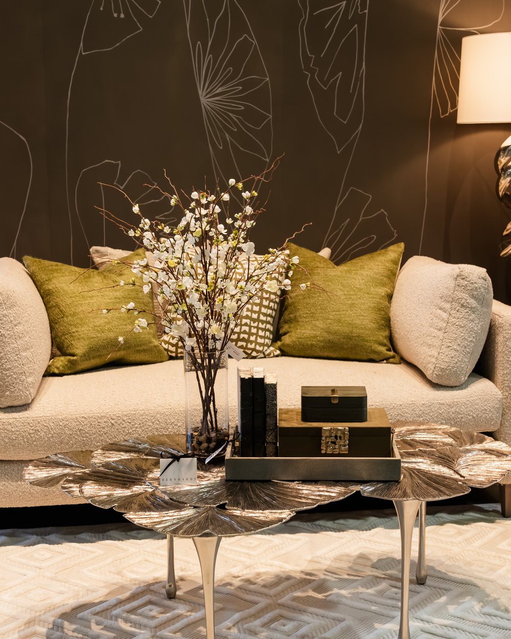 A cream sofa with olive pillows and gold lily-pad cluster tables on a patterned rug