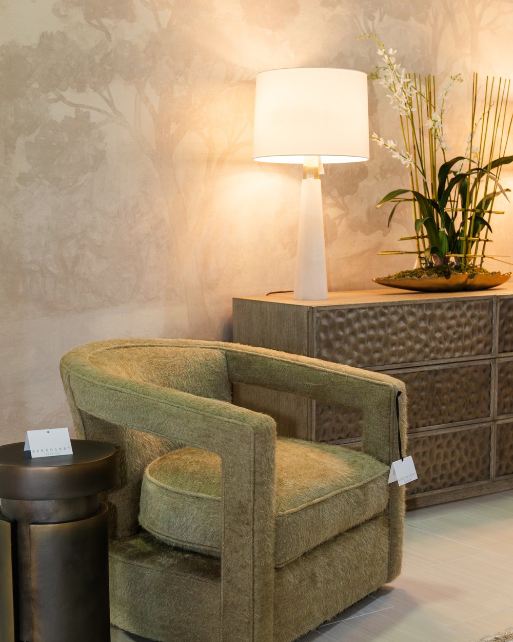 An olive boucle swivel chair beside a hammered console and lamp