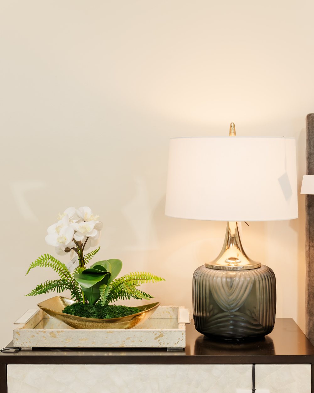 A green glass lamp beside a white orchid on a capiz-front console