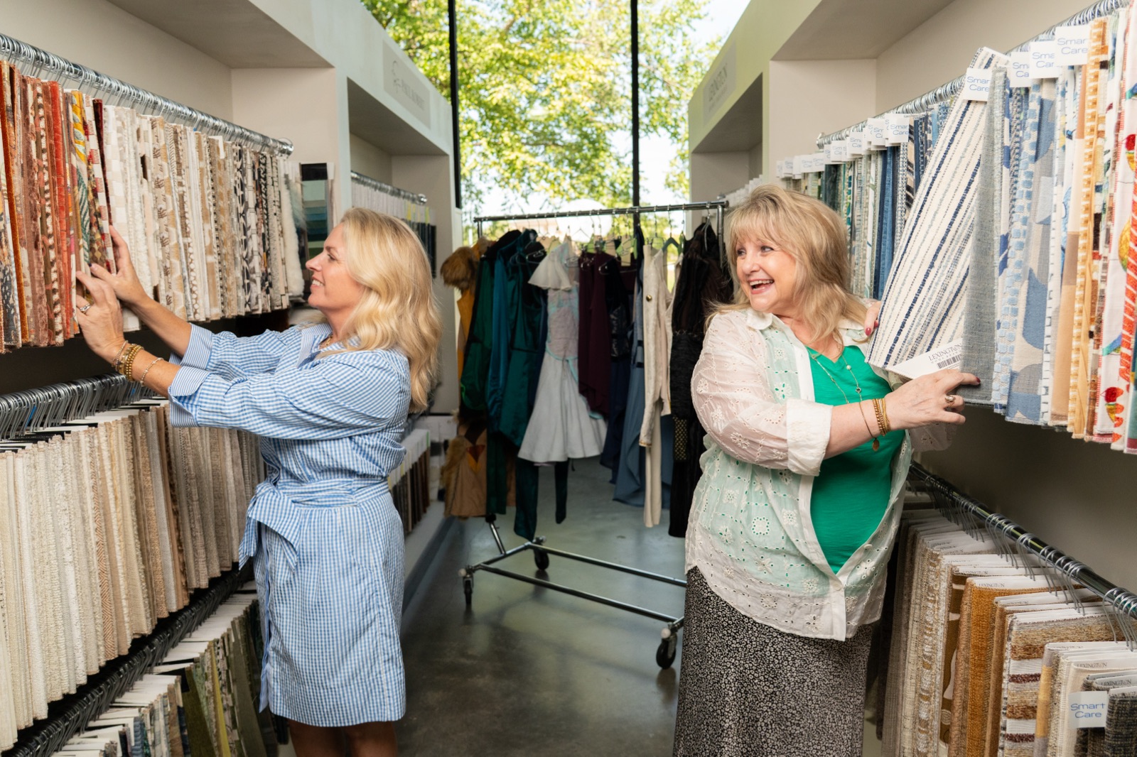 Jessica Gordon and Becky Mosby pull fabric samples from the Seville Home fabric library, with Wizard of Oz costumes on a rack behind them