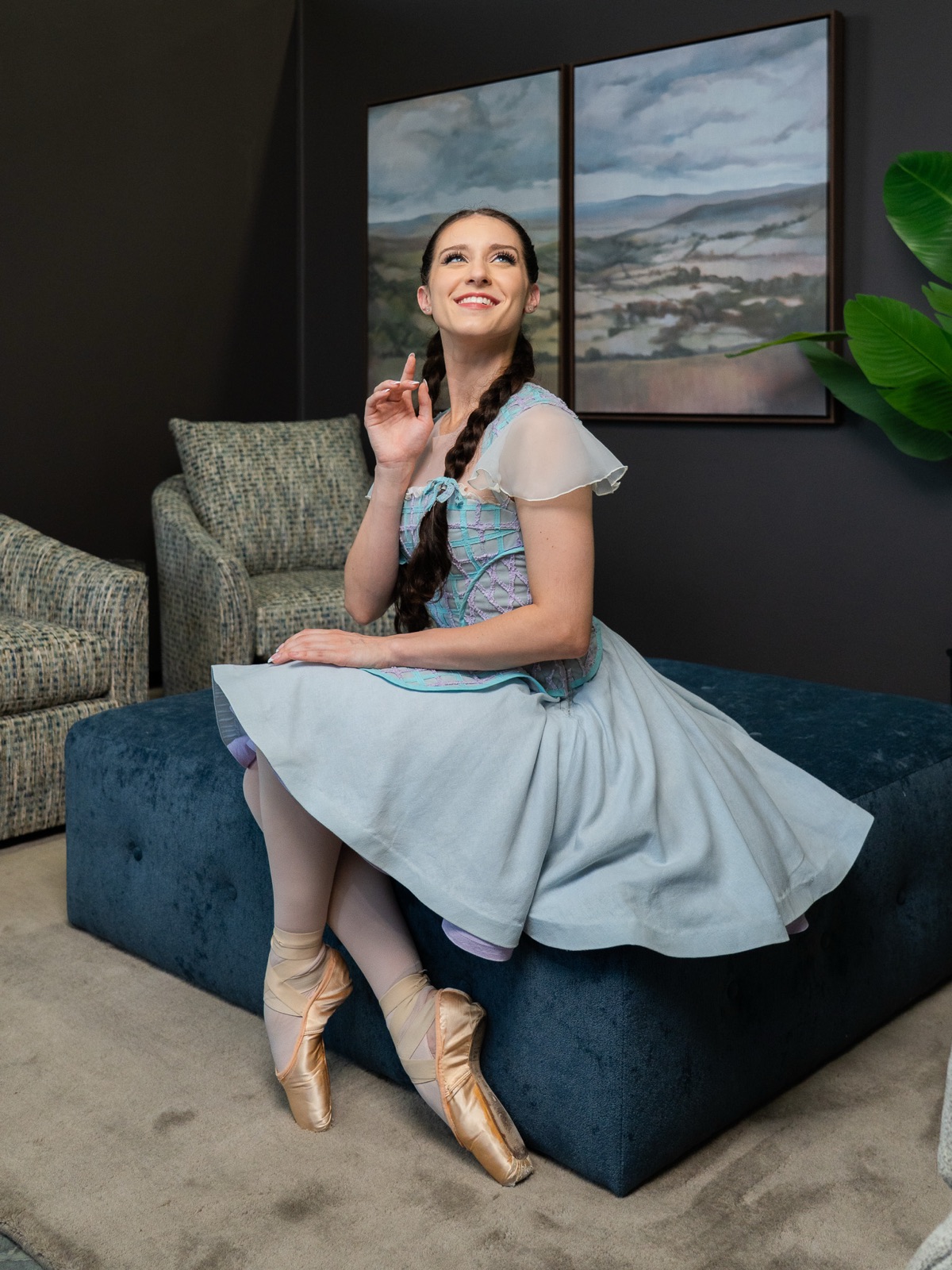 A Kansas City Ballet dancer in Dorothy's blue dress and pointe shoes, seated on a navy velvet ottoman in the Seville Home showroom