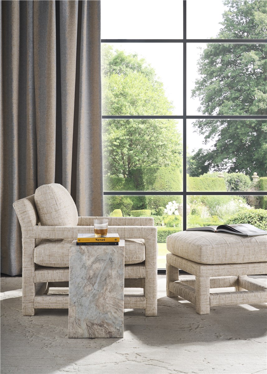 A single cream linen chair and ottoman by a tall garden window, a marble cube table with books and a glass, a calm and quiet place to simply be
