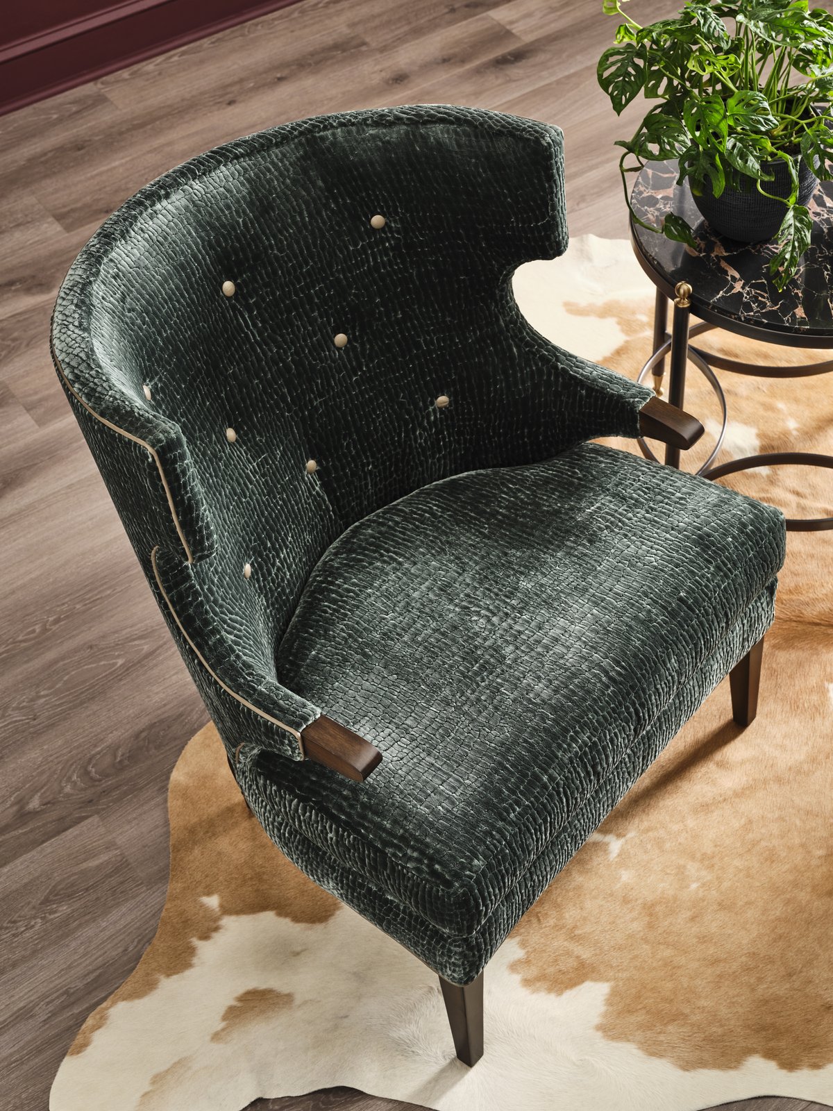 A deep teal button-tufted Massoud Pierre wing chair with wood arm caps on a cowhide rug, every small detail rich with craftsmanship