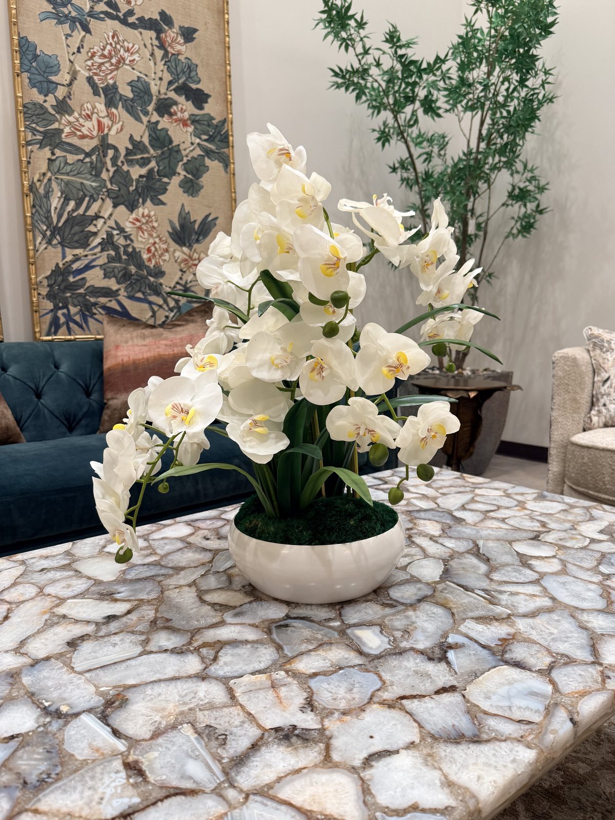 White orchids on the agate-top cocktail table in a Union Station suite, the teal Chesterfield and chinoiserie art behind