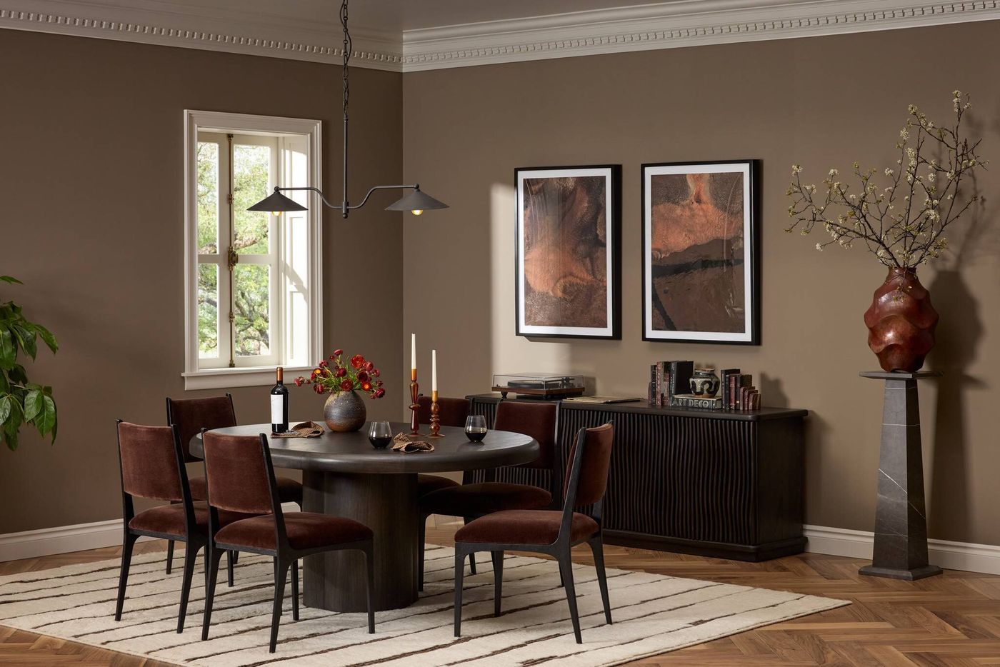 The Four Hands Pemble table opened from a round into an oval, set with velvet dining chairs in a warm taupe dining room.