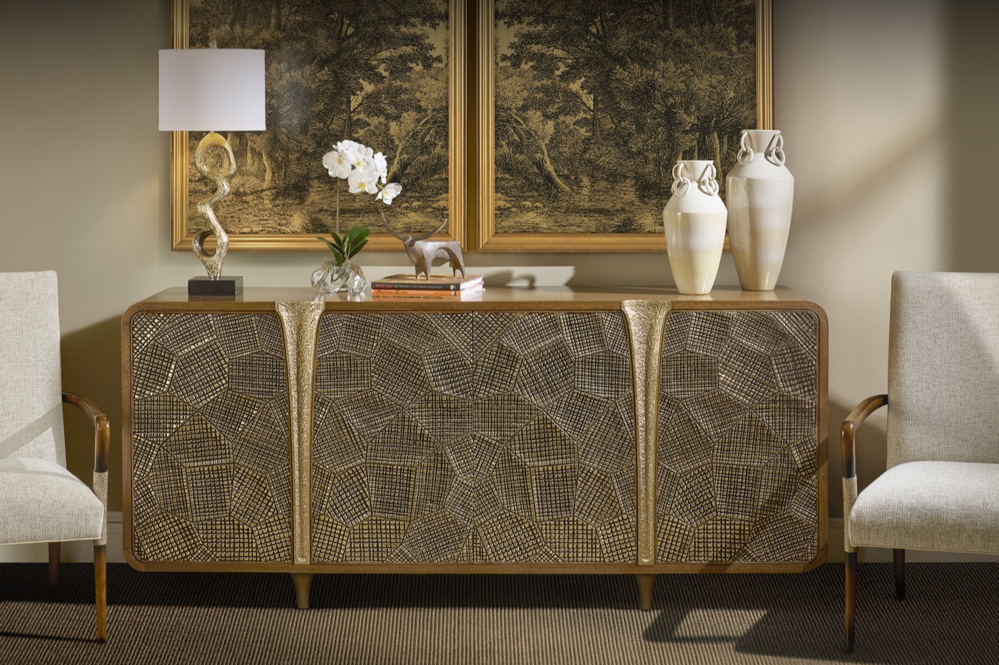 The Pathfinder four-door credenza by John-Richard, mosaic-textured gold doors with hammered pulls, styled beneath a pair of framed etchings.